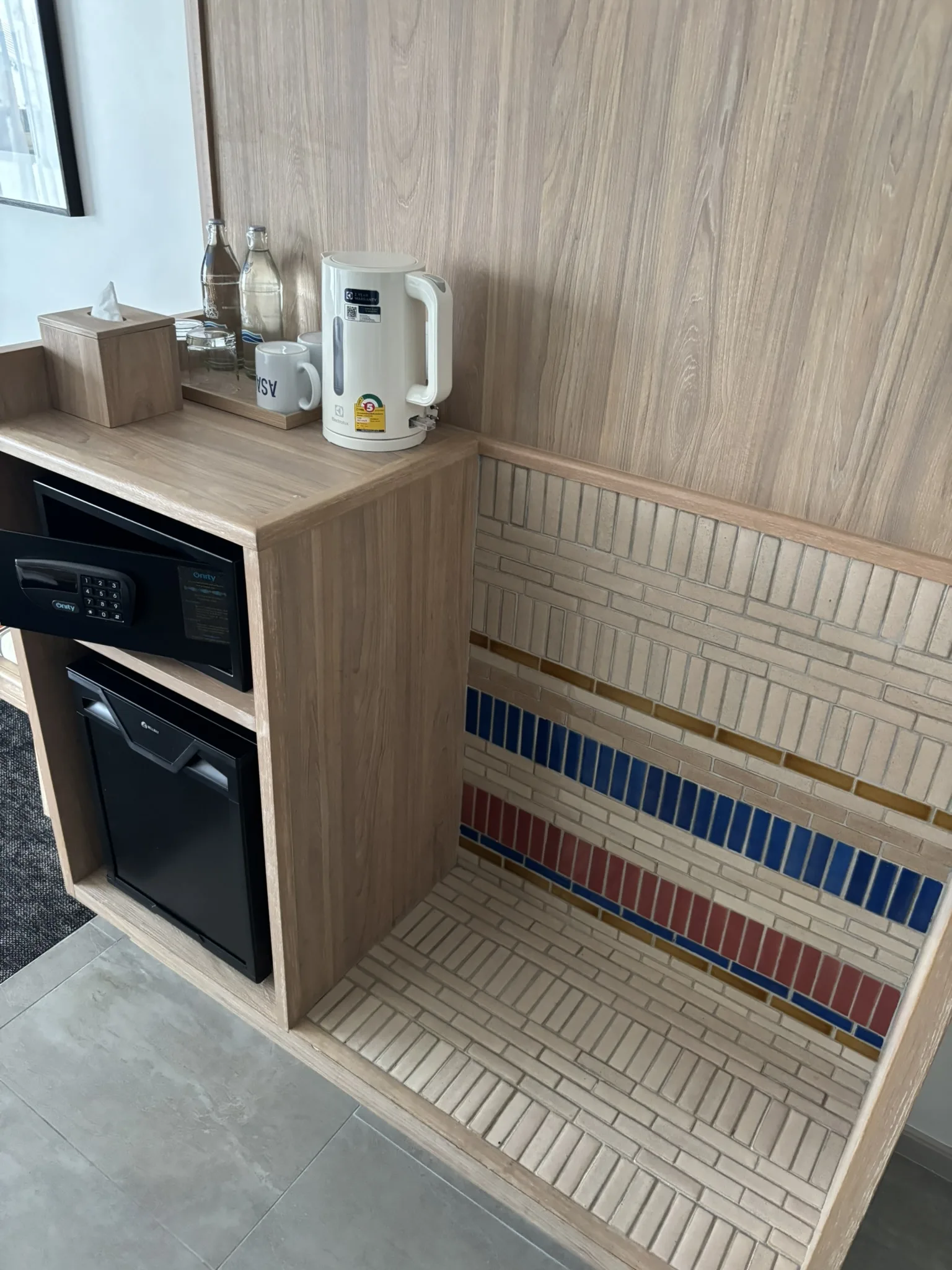 In-room amenity nook with safe, minibar, kettle, and decorative mosaic tile step at ASAI Bangkok Chinatown