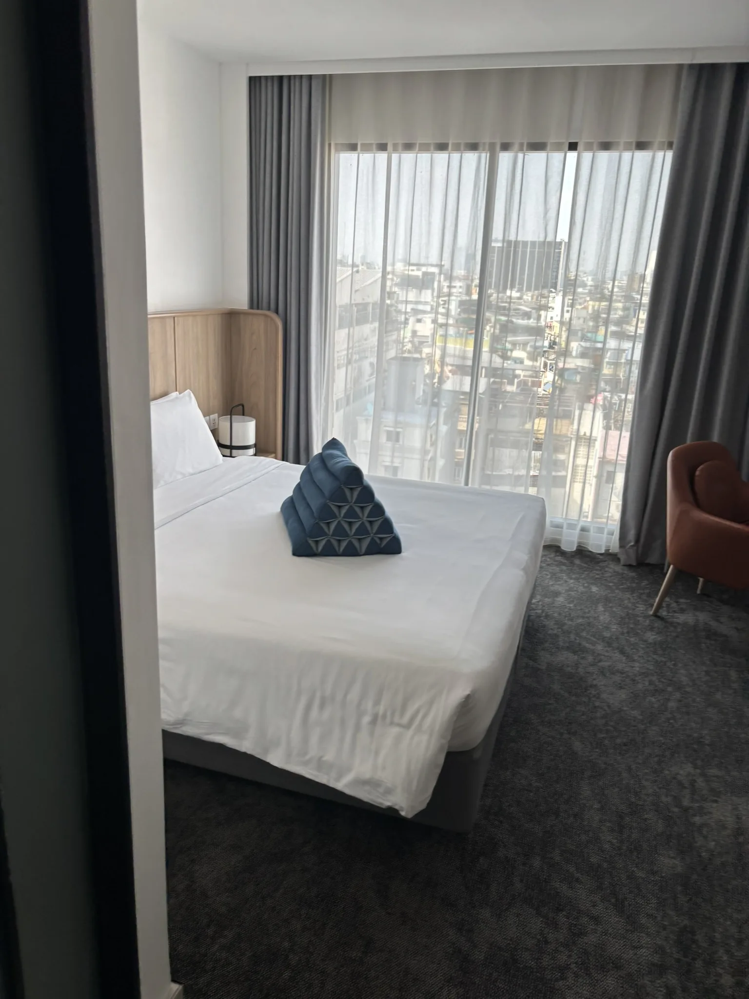 Bright hotel room at ASAI Bangkok Chinatown with a king bed, city view through sheer curtains, and armchair