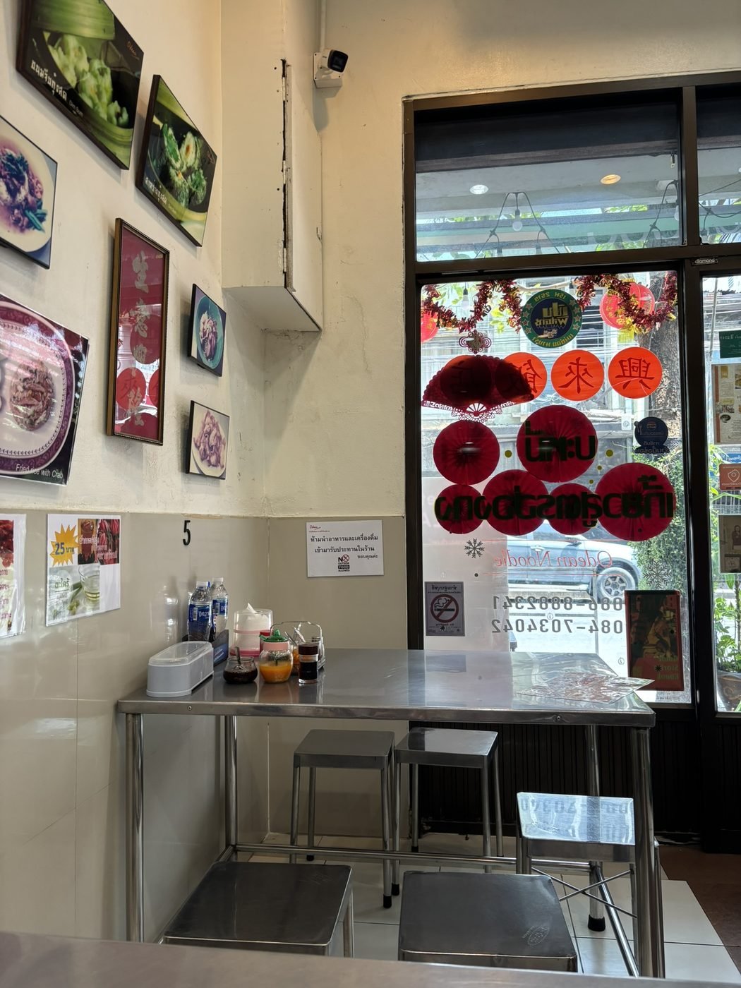 Interior of Odean Crab Wonton Noodle, Bangkok Chinatown, with framed food photos on the wall and Chinese New Year decorations in the window